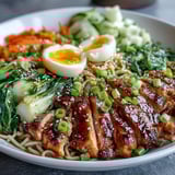 A close-up of Healthy Miso Chicken Noodle Bowls garnished with soft-boiled eggs, scallions, sesame seeds, and chili oil for extra heat.