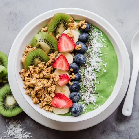 A vibrant green smoothie bowl topped with crunchy granola and fresh fruit slices for a refreshing breakfast.