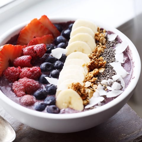 A thick acai berry smoothie bowl topped with sliced bananas, fresh blueberries, and crunchy granola for a vibrant breakfast.