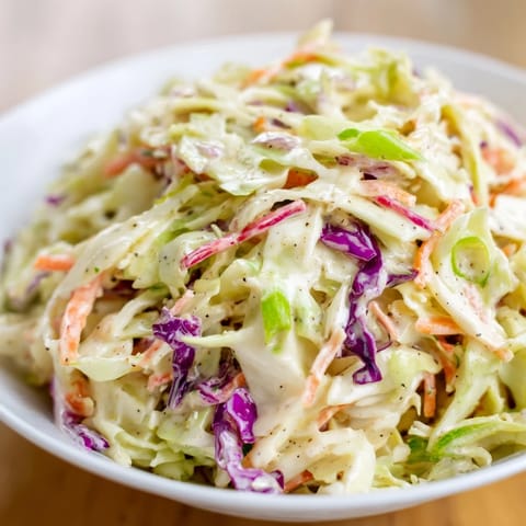 A bowl of Quick Coleslaw Salad, with grated carrots and green onions in creamy dressing, ready to enjoy.