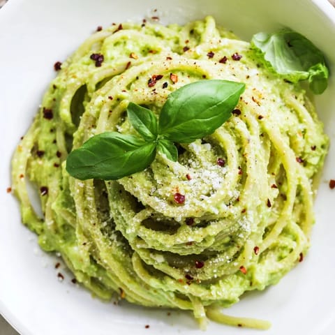 Vibrant green smashed avocado pasta served in a ceramic bowl, garnished with chili flakes and a drizzle of olive oil.  