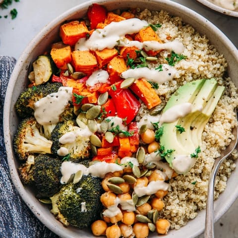 Close-up view of a Quinoa Buddha Bowl featuring roasted vegetables, hearty legumes, and a drizzle of rich tahini dressing over fluffy quinoa.
