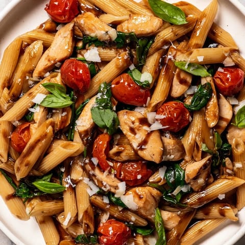 A vibrant plate of Balsamic Glazed Chicken Pasta features golden-brown chicken strips, al dente penne, and glistening cherry tomatoes, ready to serve.