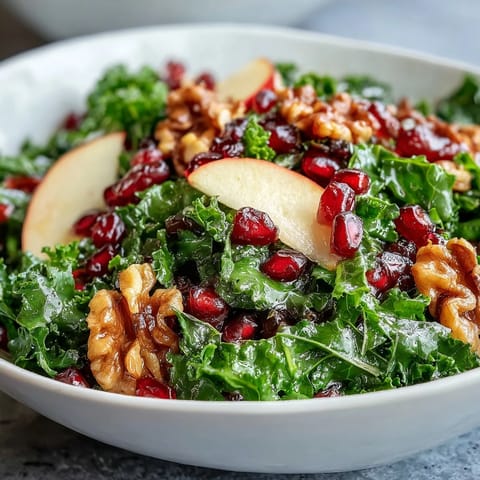 A vibrant bowl of kale, crisp apple slices, and ruby pomegranate seeds topped with chopped walnuts.