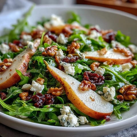 Fresh Arugula and Pear Bowl salad topped with crumbled blue cheese and toasted walnuts on a white ceramic plate. 