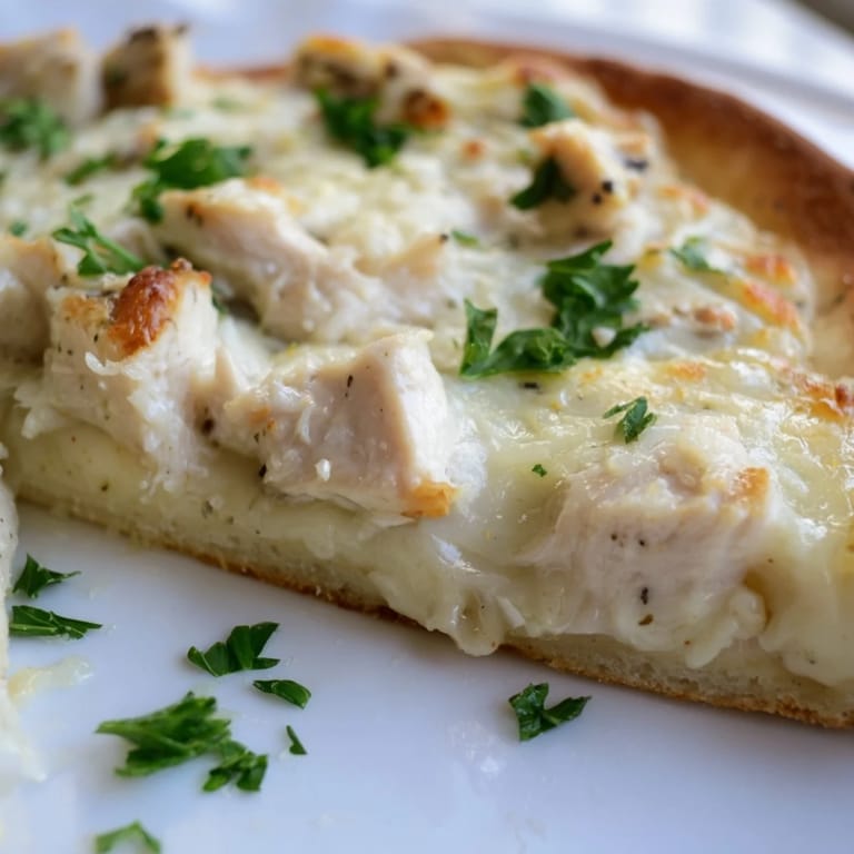 Perfectly baked Chicken Alfredo Pizza garnished with fresh parsley, featuring a golden crust and bubbly cheese for a comforting family dinner.