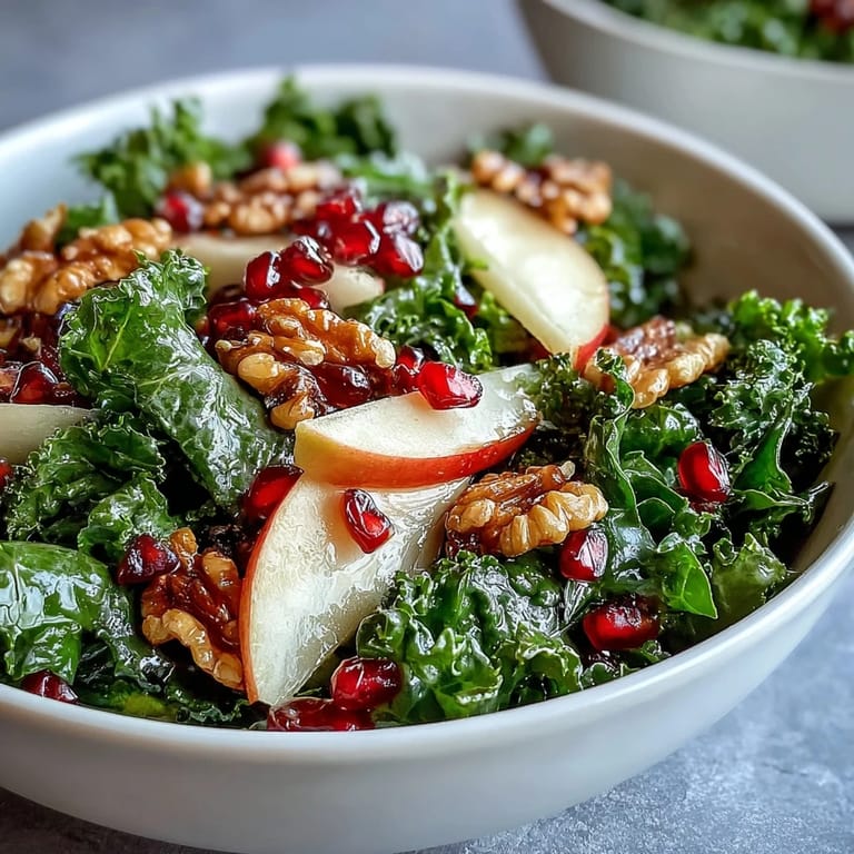 Healthy gluten-free kale and pomegranate salad bowl tossed with sliced apples and a sweet honey mustard dressing.